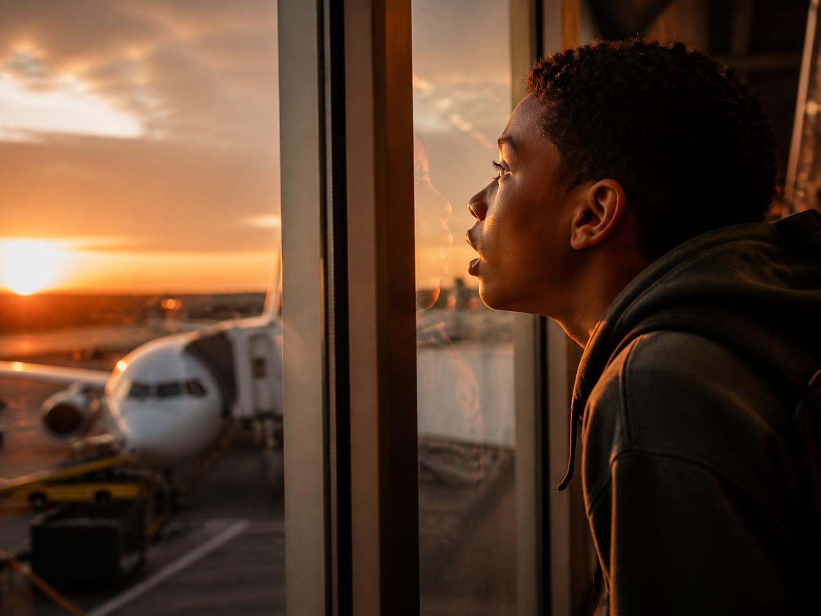 A teenager watching a jet from an airport terminal window at sunrise
